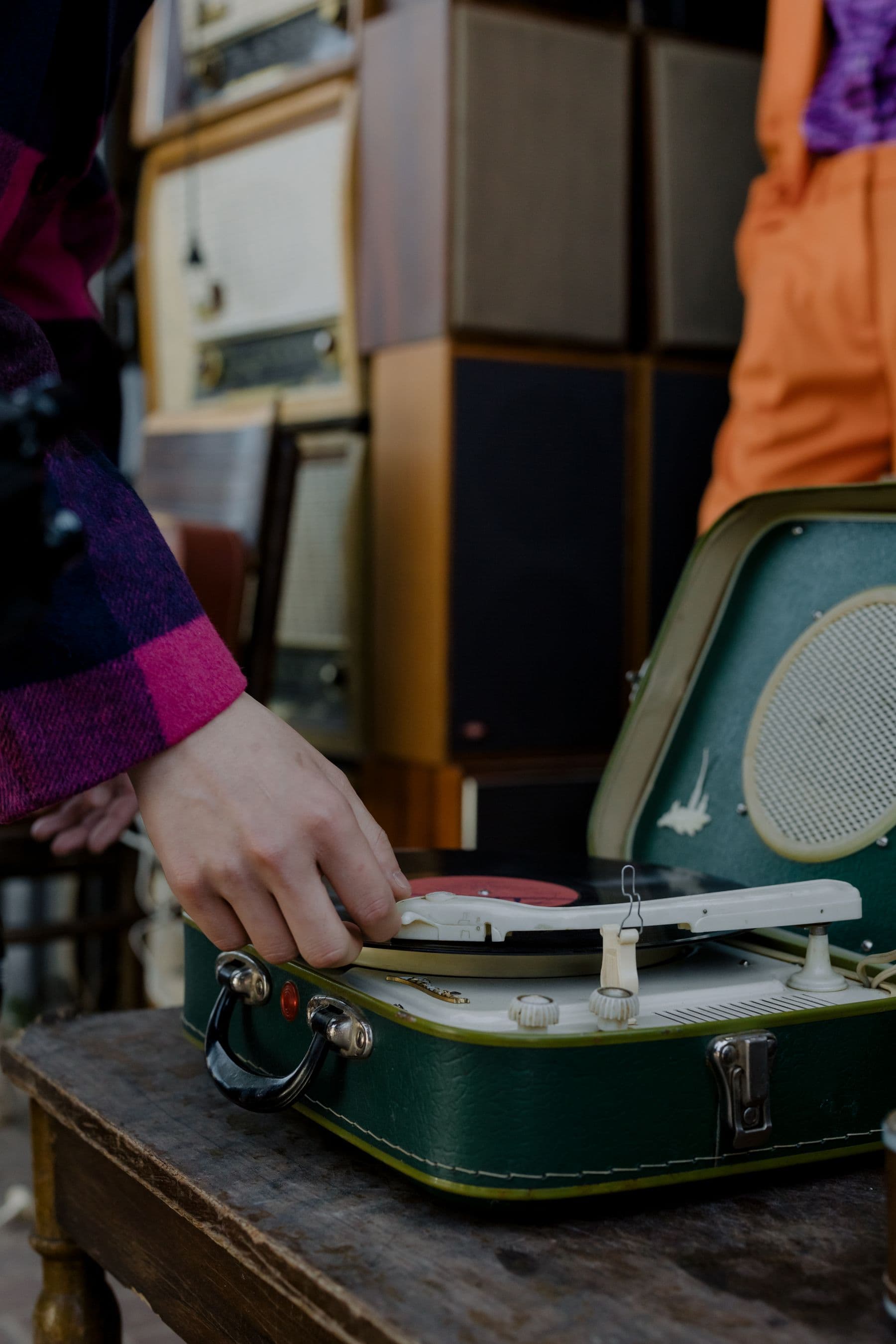A hand adjusts the tonearm on a worn green record player